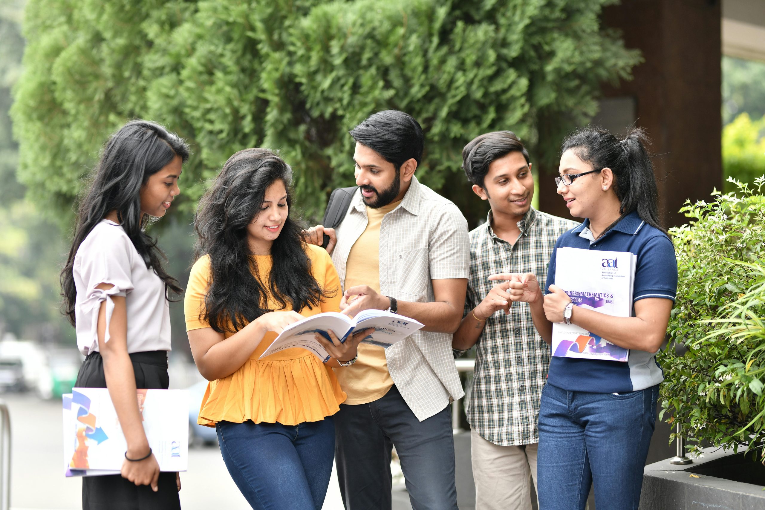 A group of diverse college students engaged in outdoor group study session, sharing books and ideas.